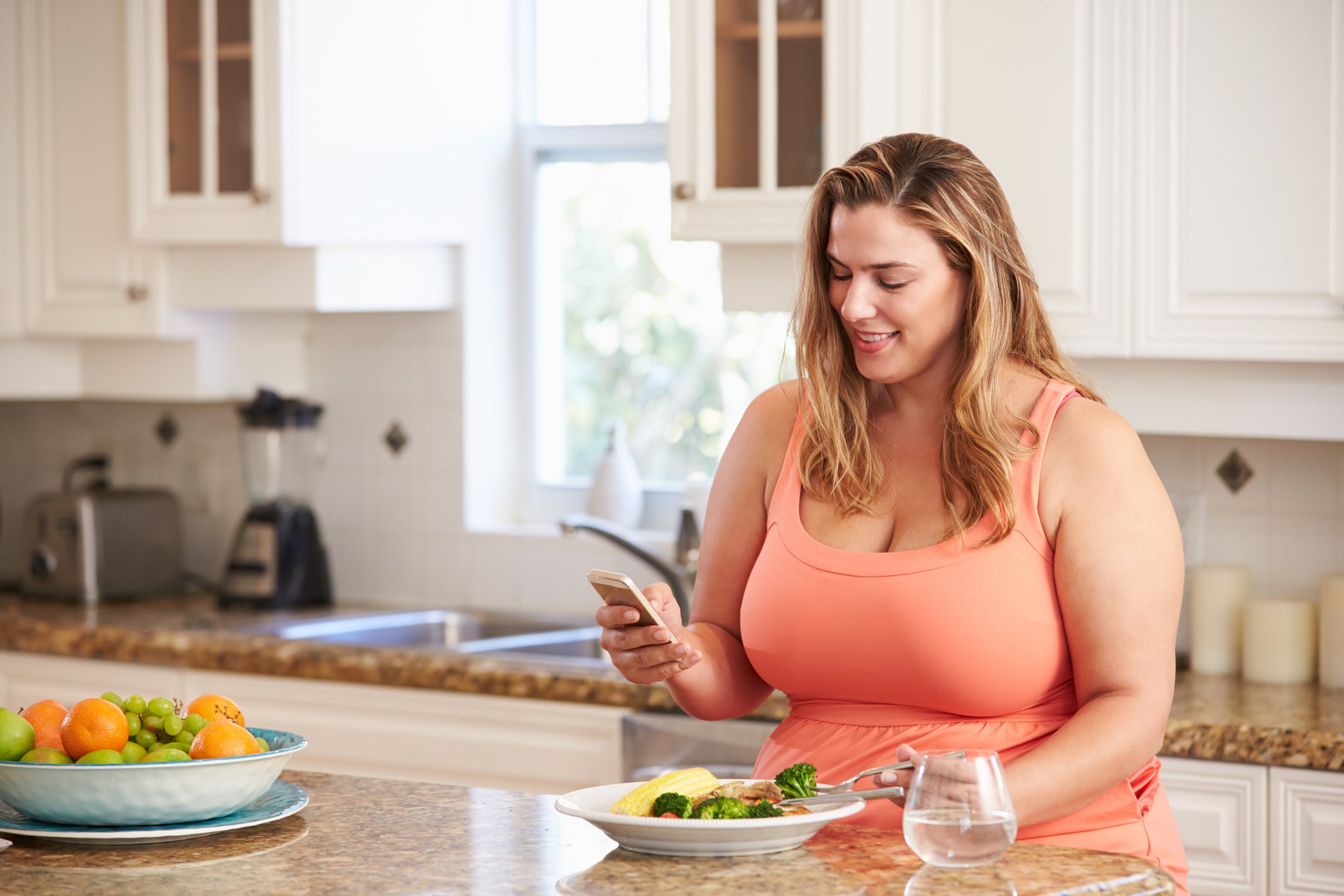 Overweight Woman Eating Healthy Meal And Using Mobile Phone.