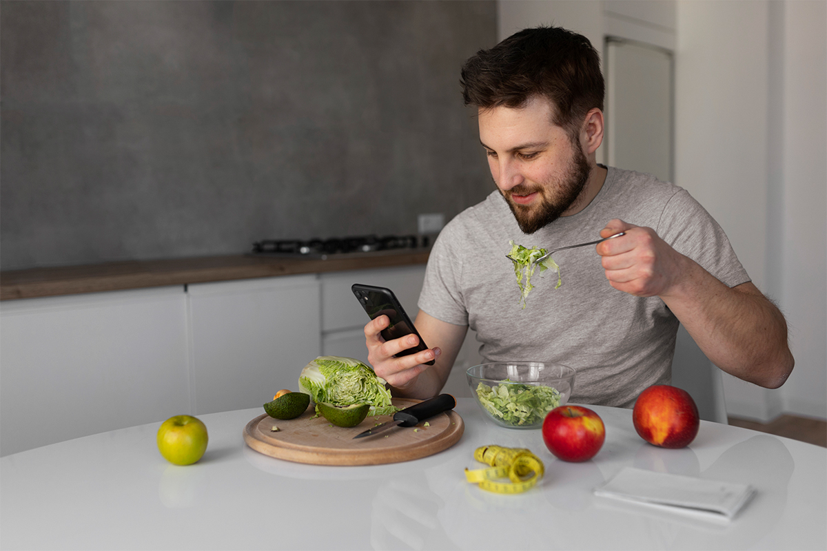 Young man eating and checking his smartphone.